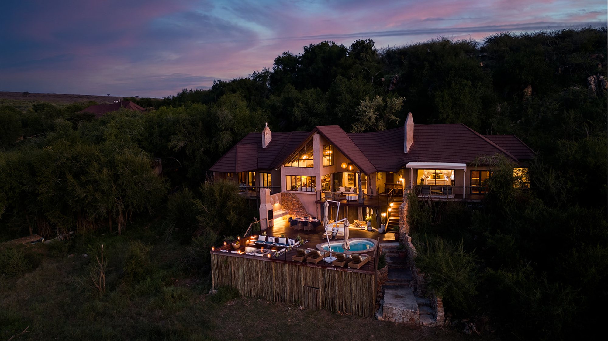 A safari lodge lit up at dusk, every window glowing